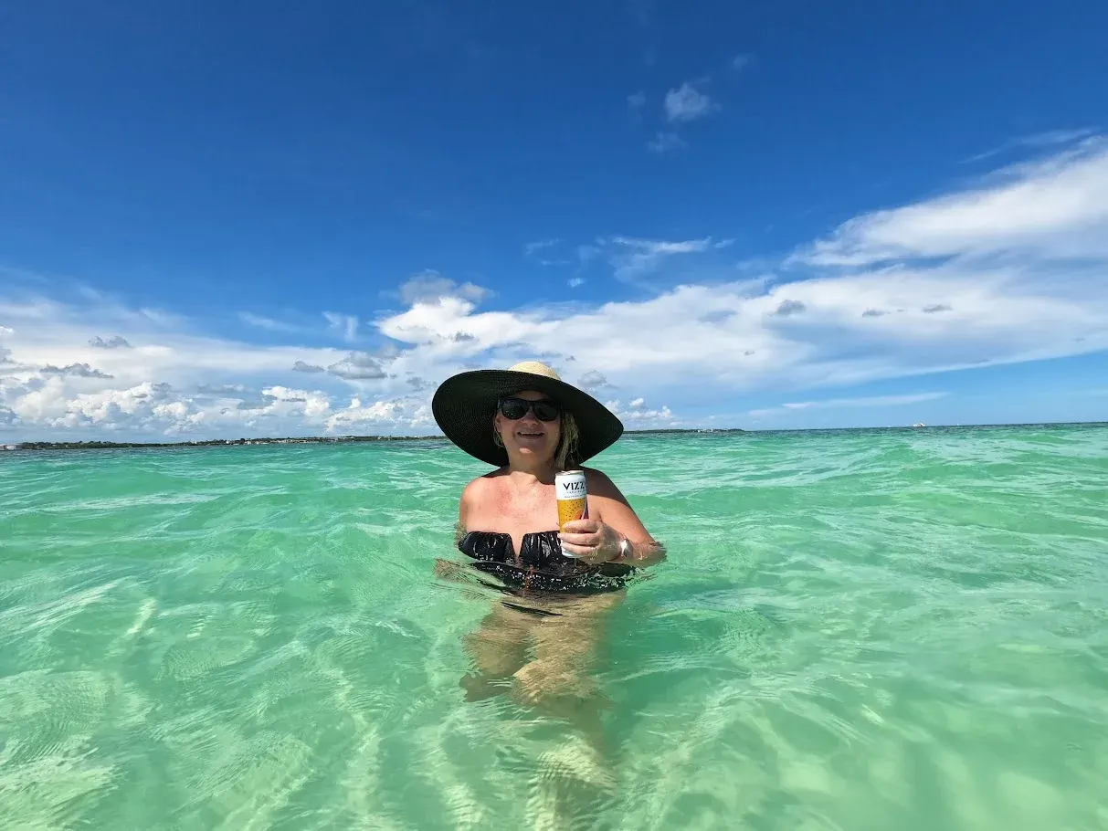Guest in a sun hat smiling in the water with a drink