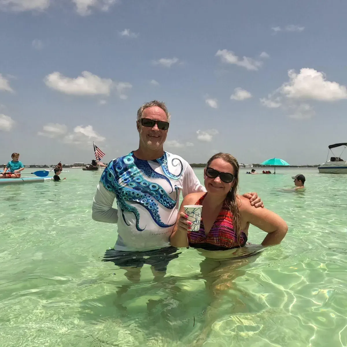 A couple smiling while standing in waist-deep turquoise water at the Islamorada sandbar