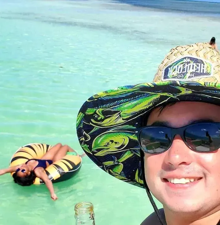 A smiling guest in a sun hat enjoying a drink while another relaxes on a float in the clear Islamorada water