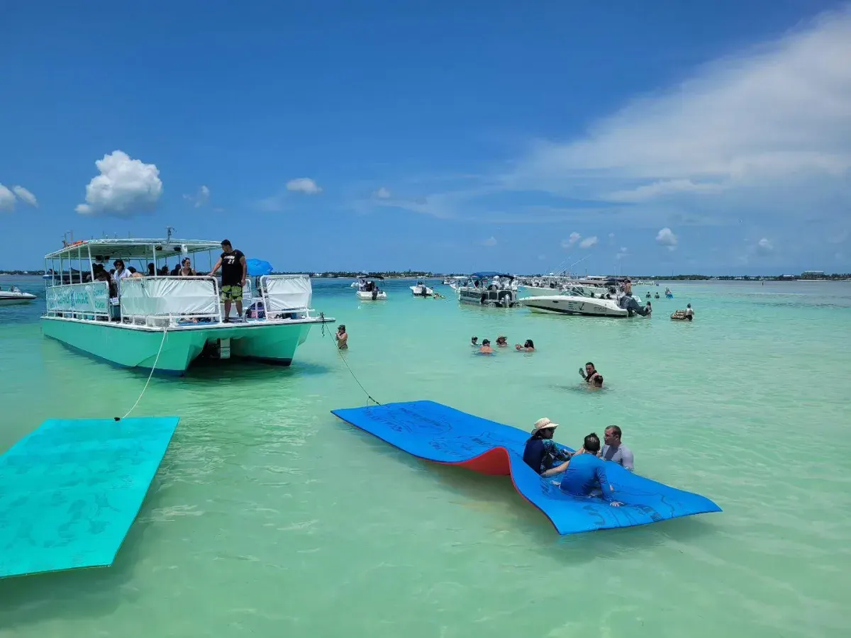 Guests sitting on large blue and teal floating mats behind a Clearly Unique Charters boat in shallow water