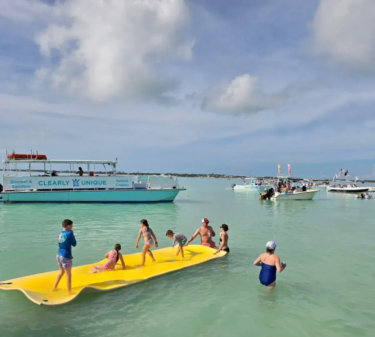Kids on a yellow floating mat at the sandbar with a Clearly Unique Charters boat behind