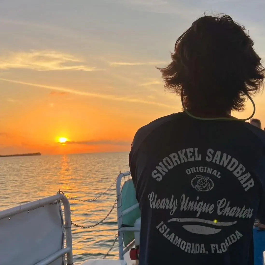 Guest in a Clearly Unique Charters shirt watching the sunset from the boat